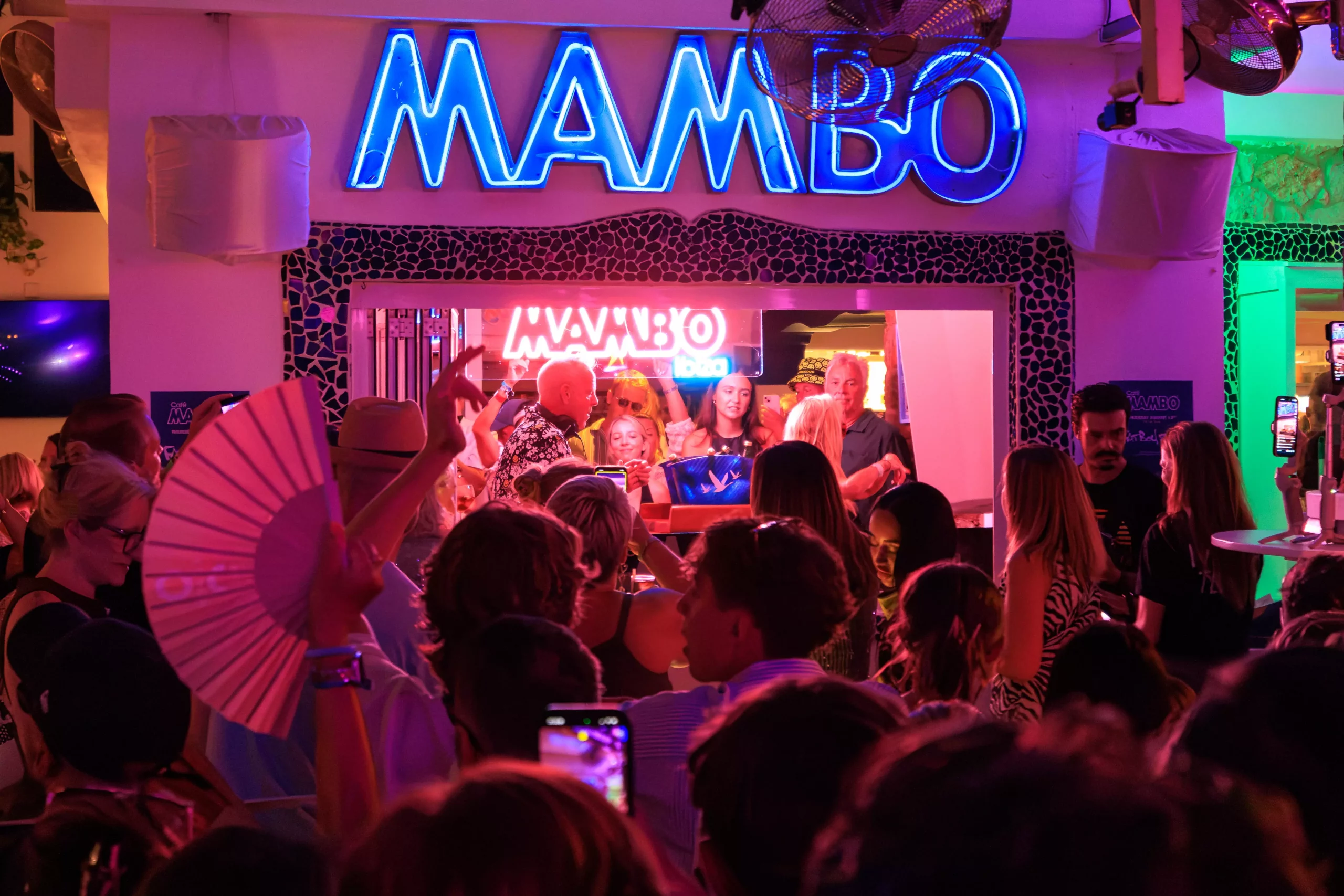 Crowds dancing beneath the neon Café Mambo sign during a sunset set in San Antonio, Ibiza